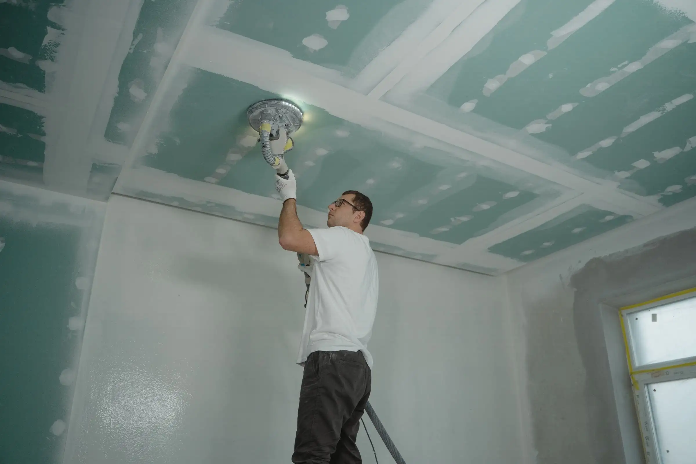 Worker sanding a drywall ceiling