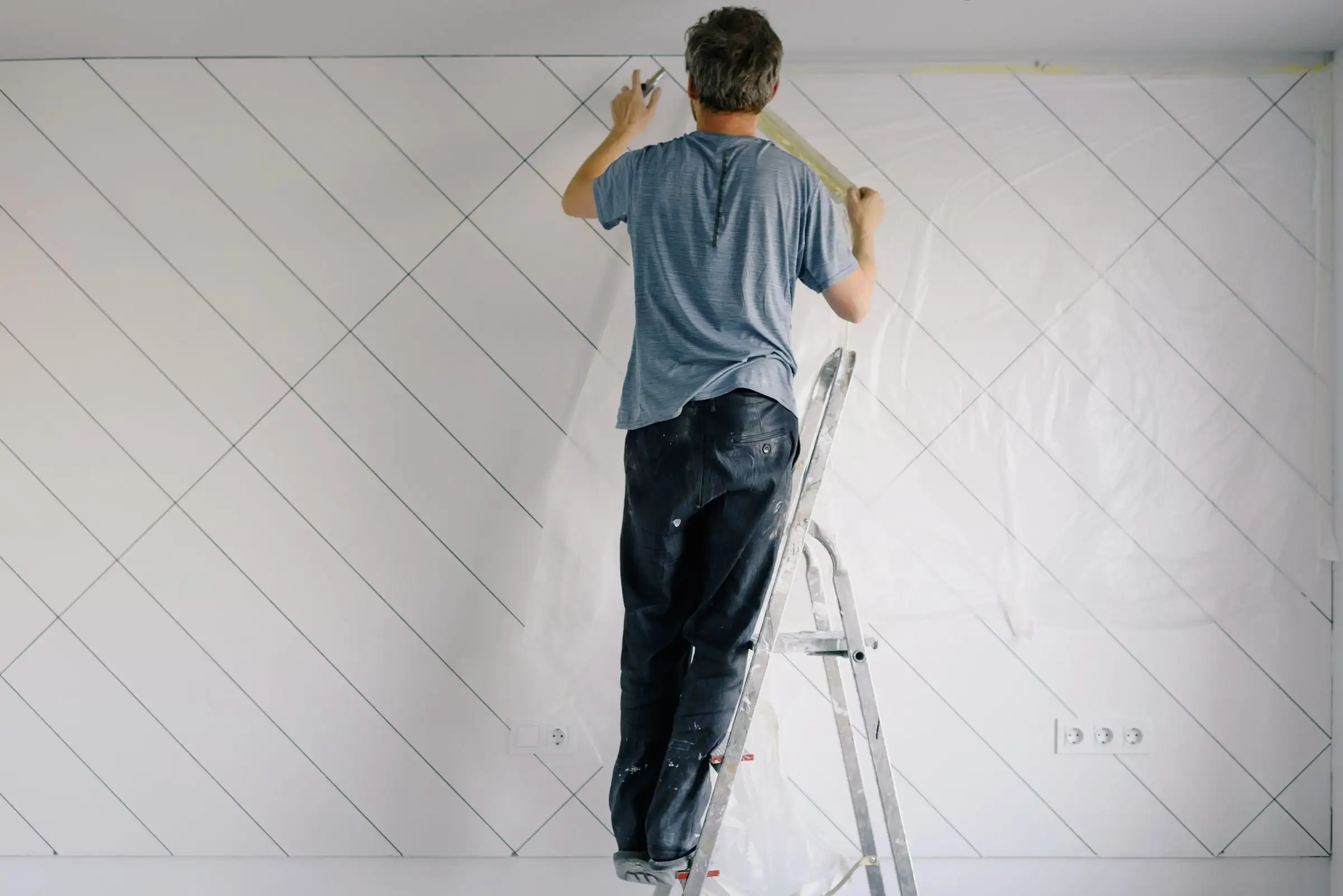 Painter on a ladder painting a bright white wall