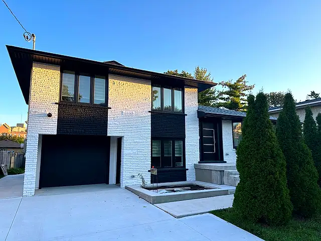 The same house front after painting: white brick with black vertical accent panels and trim