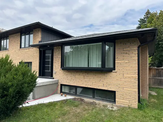 Single-storey tan brick wing with a large picture window beside the front entrance, before painting