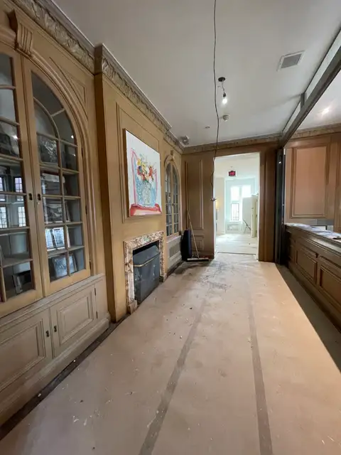 Long library room with orange-toned wood panelling, arched glass cabinets and a fireplace
