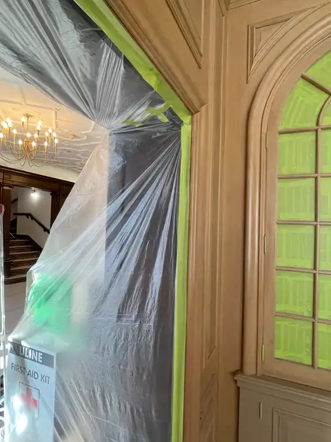 Arched cabinet and doorway masked with plastic and green tape before spraying
