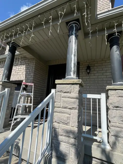 Front porch with worn, peeling black columns on stone bases